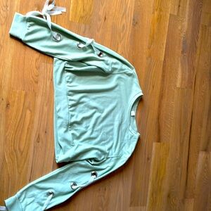 It is a cropped, light sage green sweater with little metal rings and a ribbon.